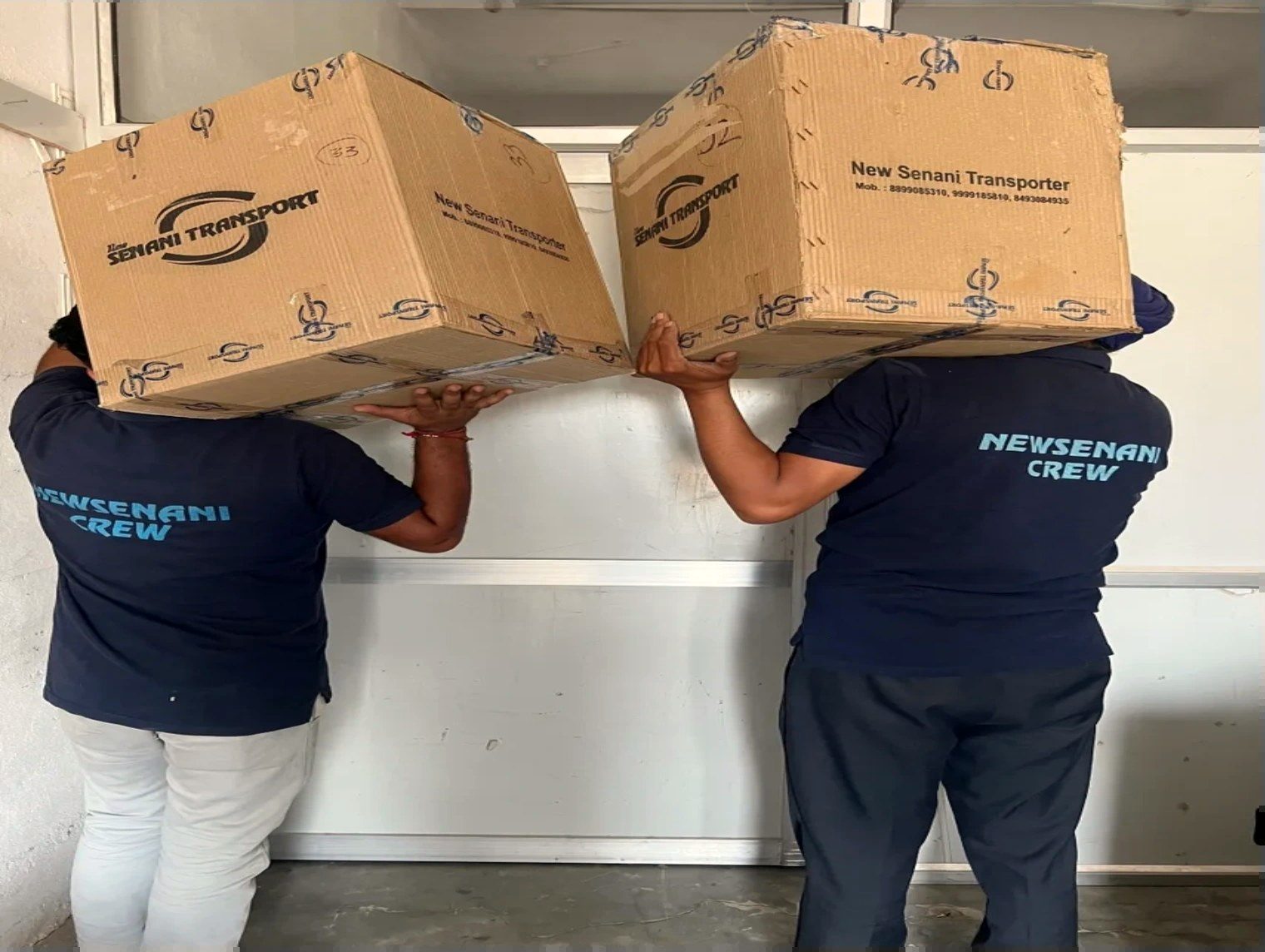 Two New Senani crew members in branded navy polos carrying company-printed moving cartons